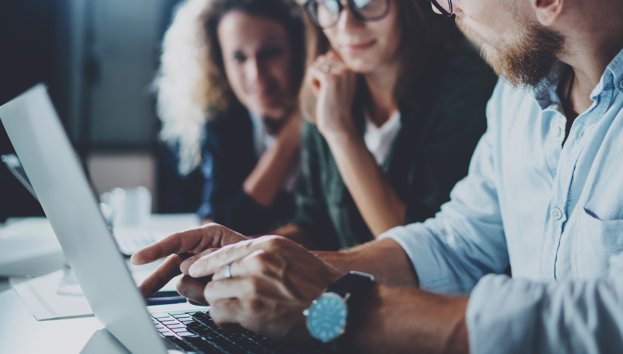 a man and two women sit at a desk with a laptop open