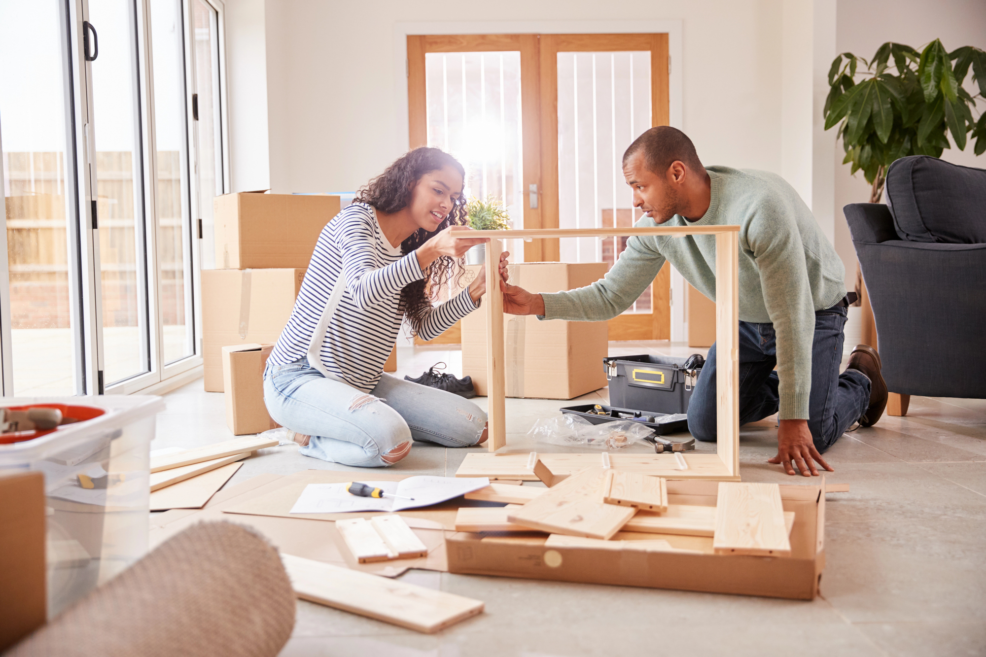 Young man and woman of color put together a piece of furniture surrounded by moving boxes.