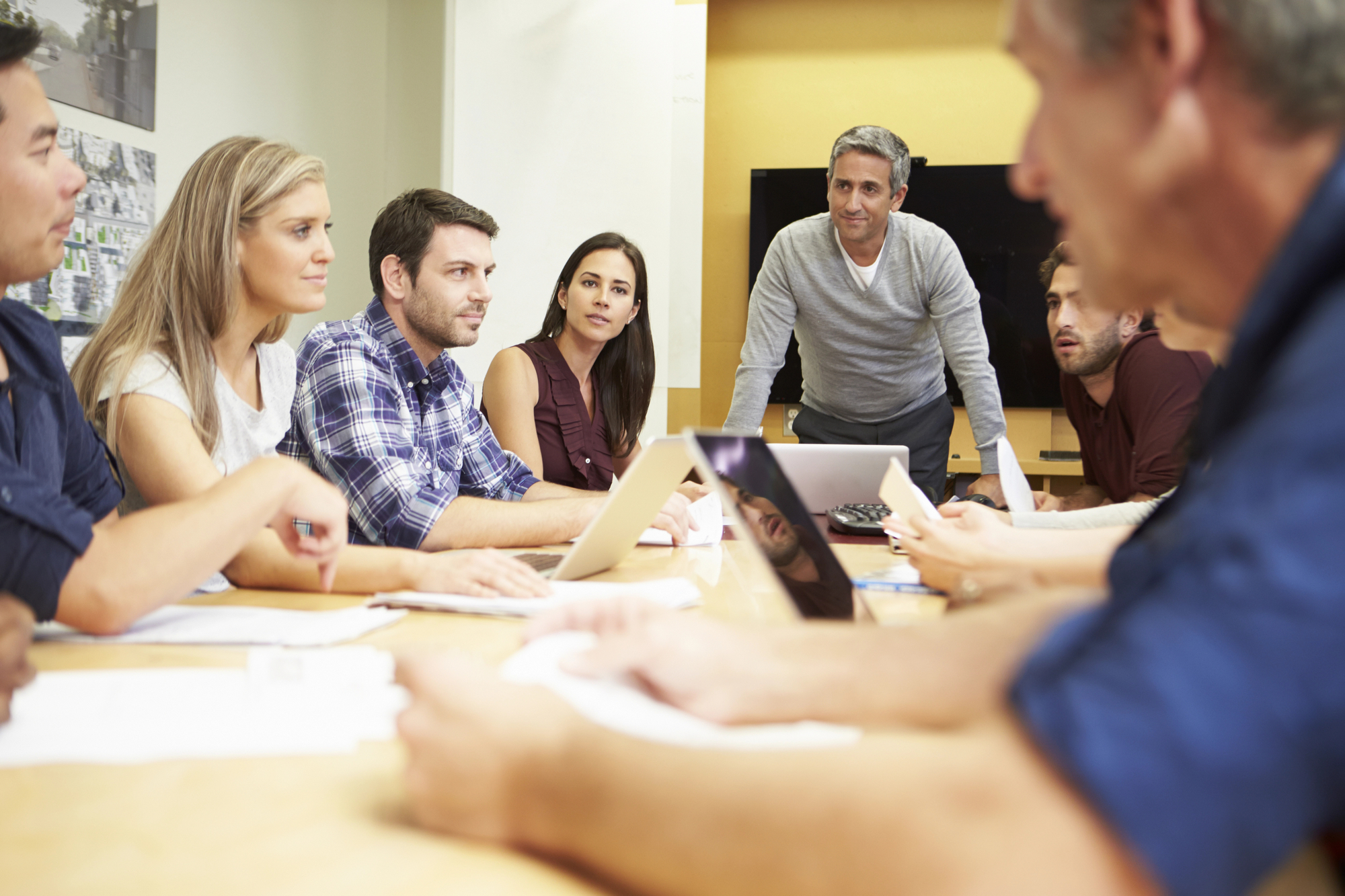 a group of people sit and stand around a table and are in conversation