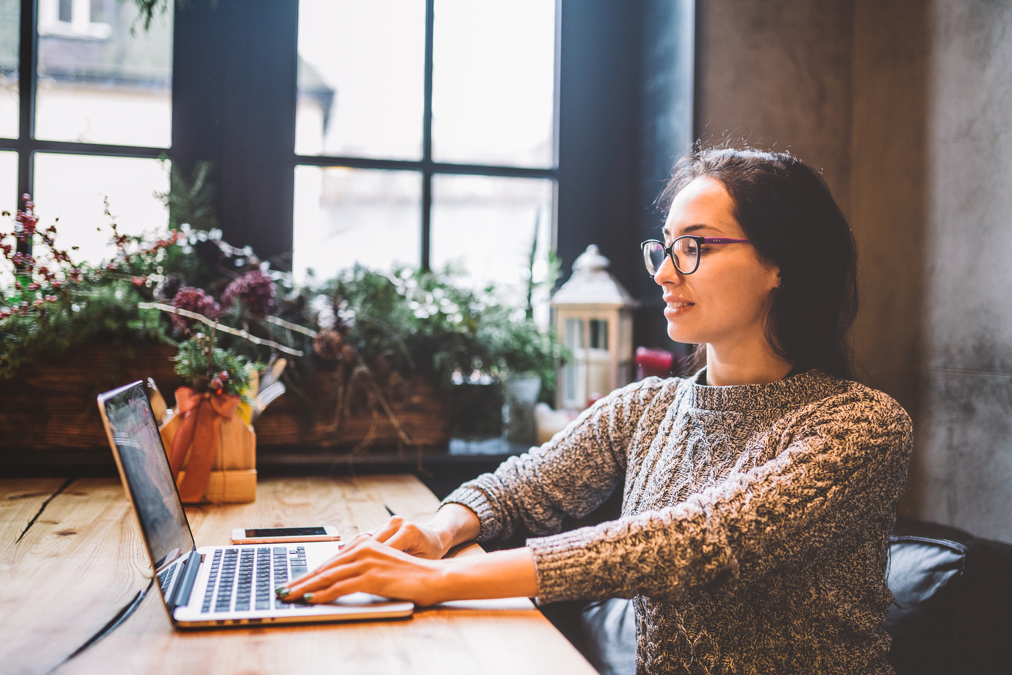 a brunette with glasses sits behind a table with a laptop working