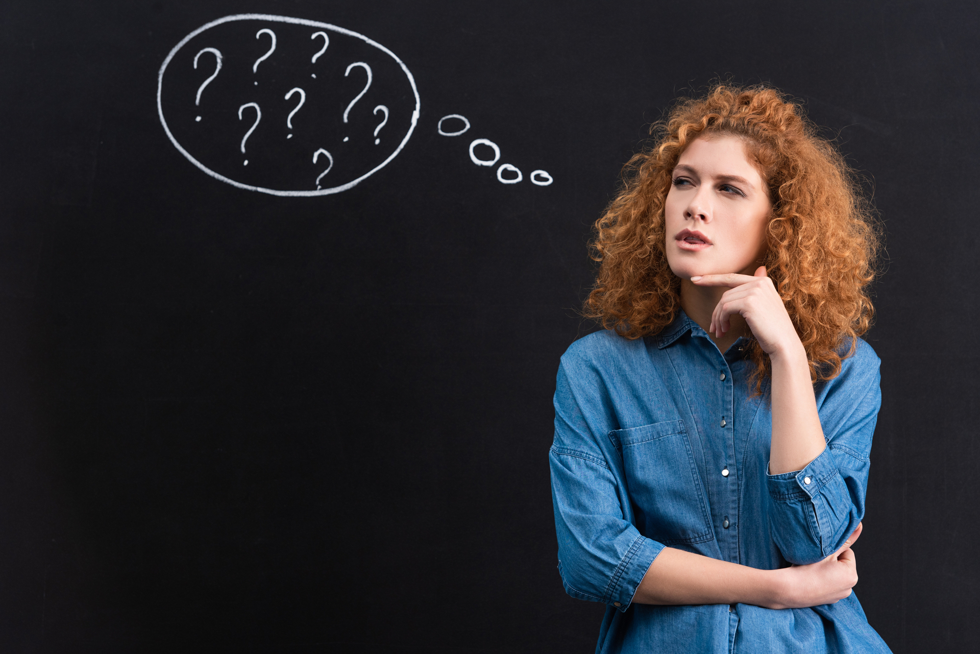 A red-haired woman against the background of a blackboard with question marks on it