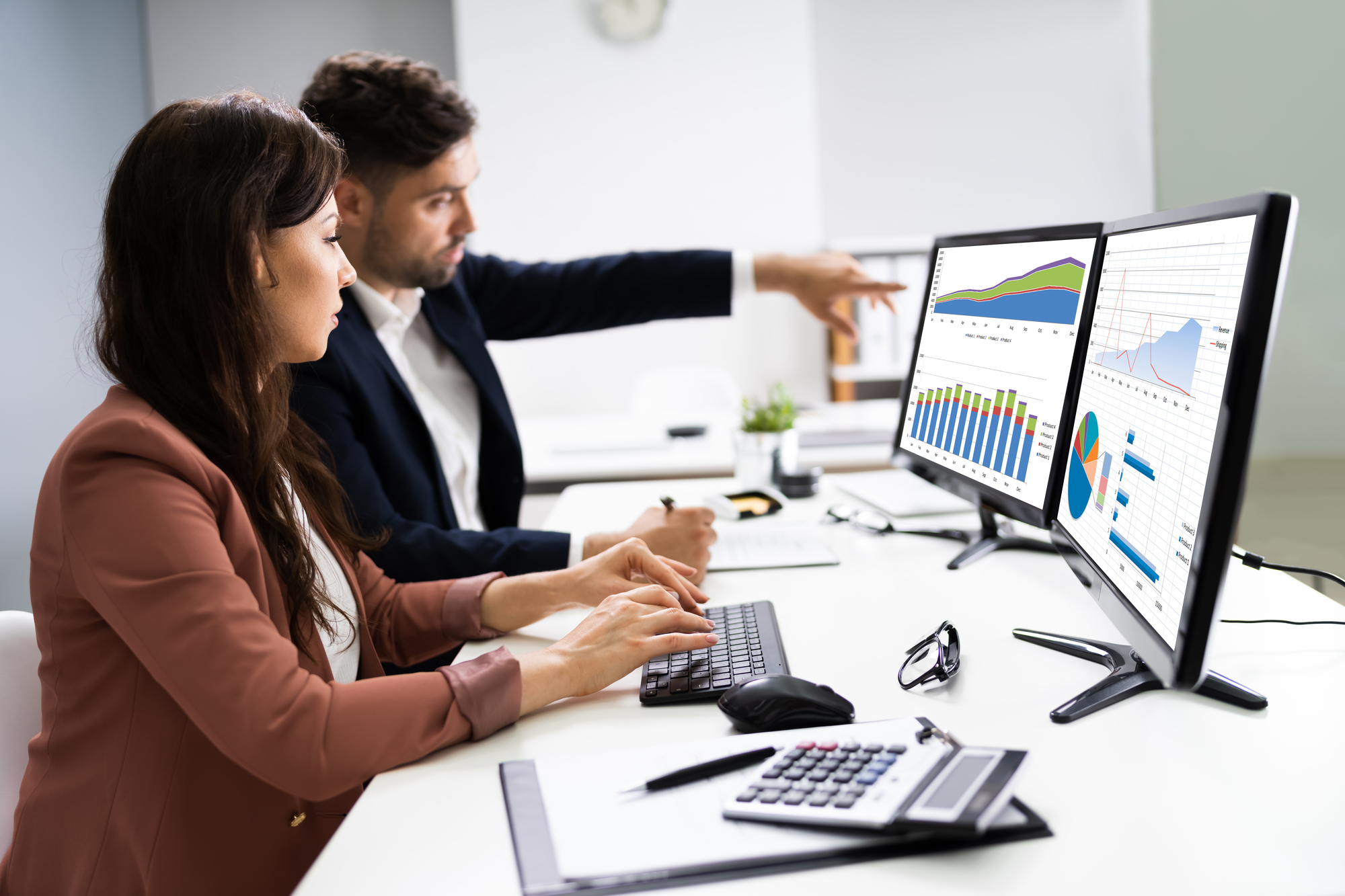 a man and a woman behind two monitors with charts