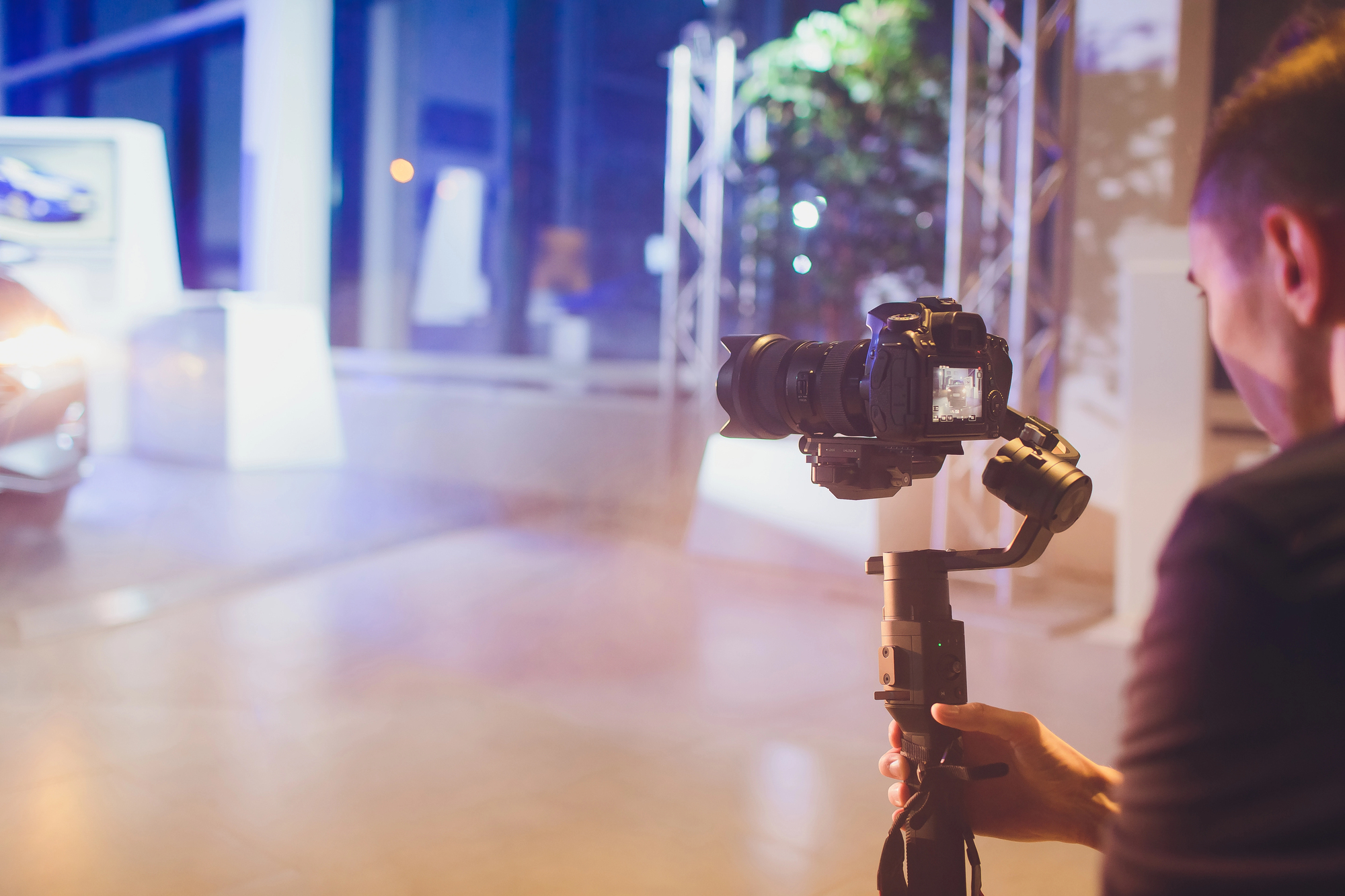 Professional videographer films with a DSLR camera on a gimbal stabilizer in a lit room.