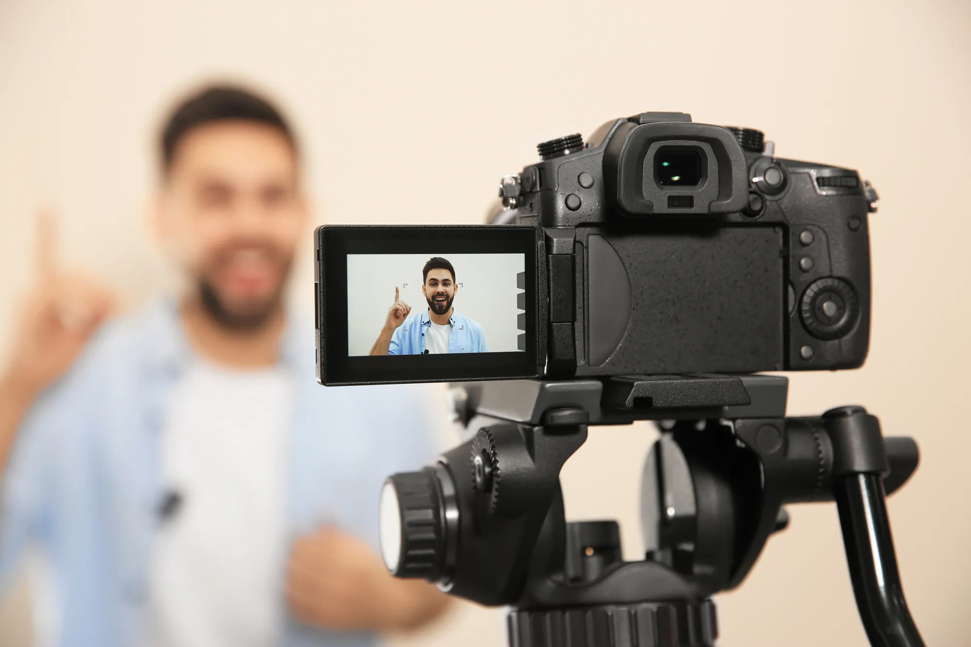 Digital camera on tripod with LCD screen showing a male speaker recording a video.