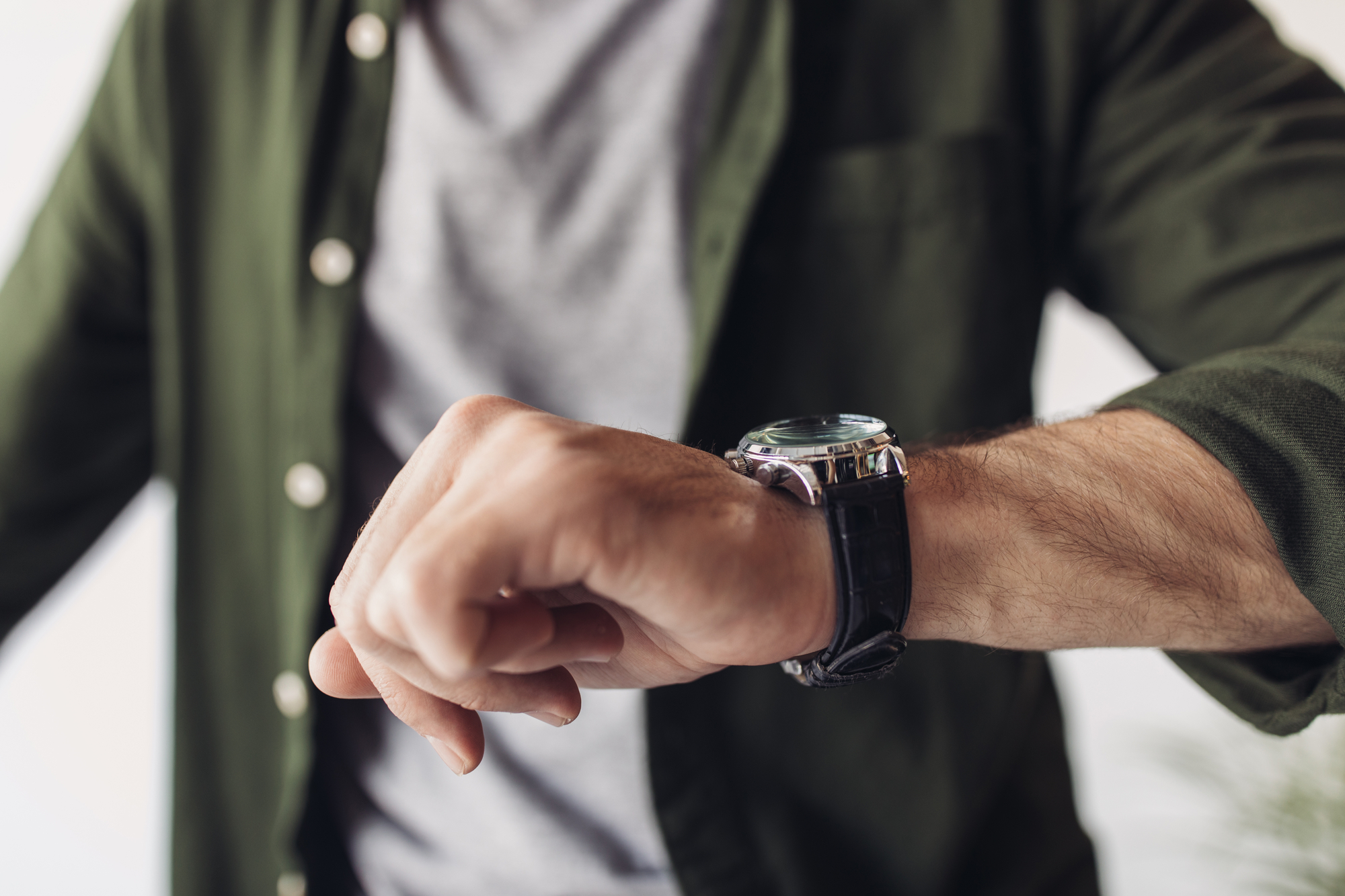 man with gray shirt and green vest looks at watch